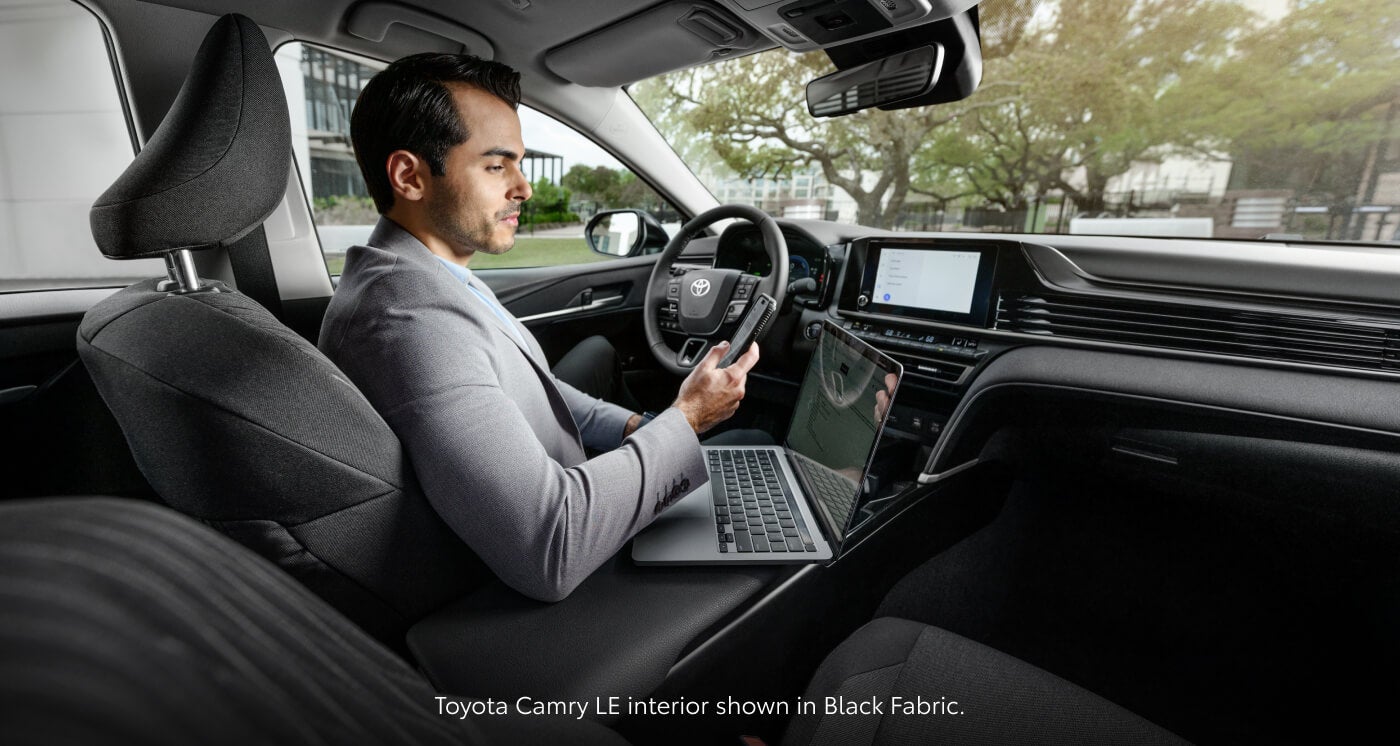 Interior view of a man sitting inside a 2026 Toyota Camry LE featuring Black Fabric seats.
