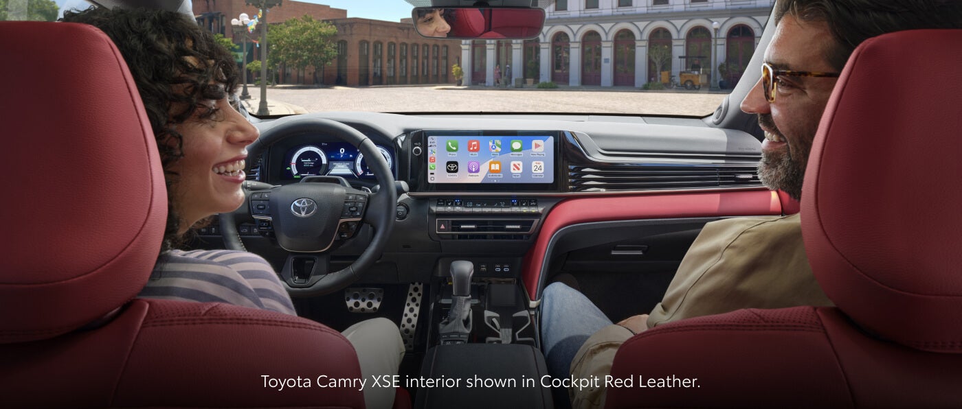 Interior view of driver and front passenger sitting in a 2026 Toyota Camry XSE featuring Cockpit Red leather seats and digital infotainment display.