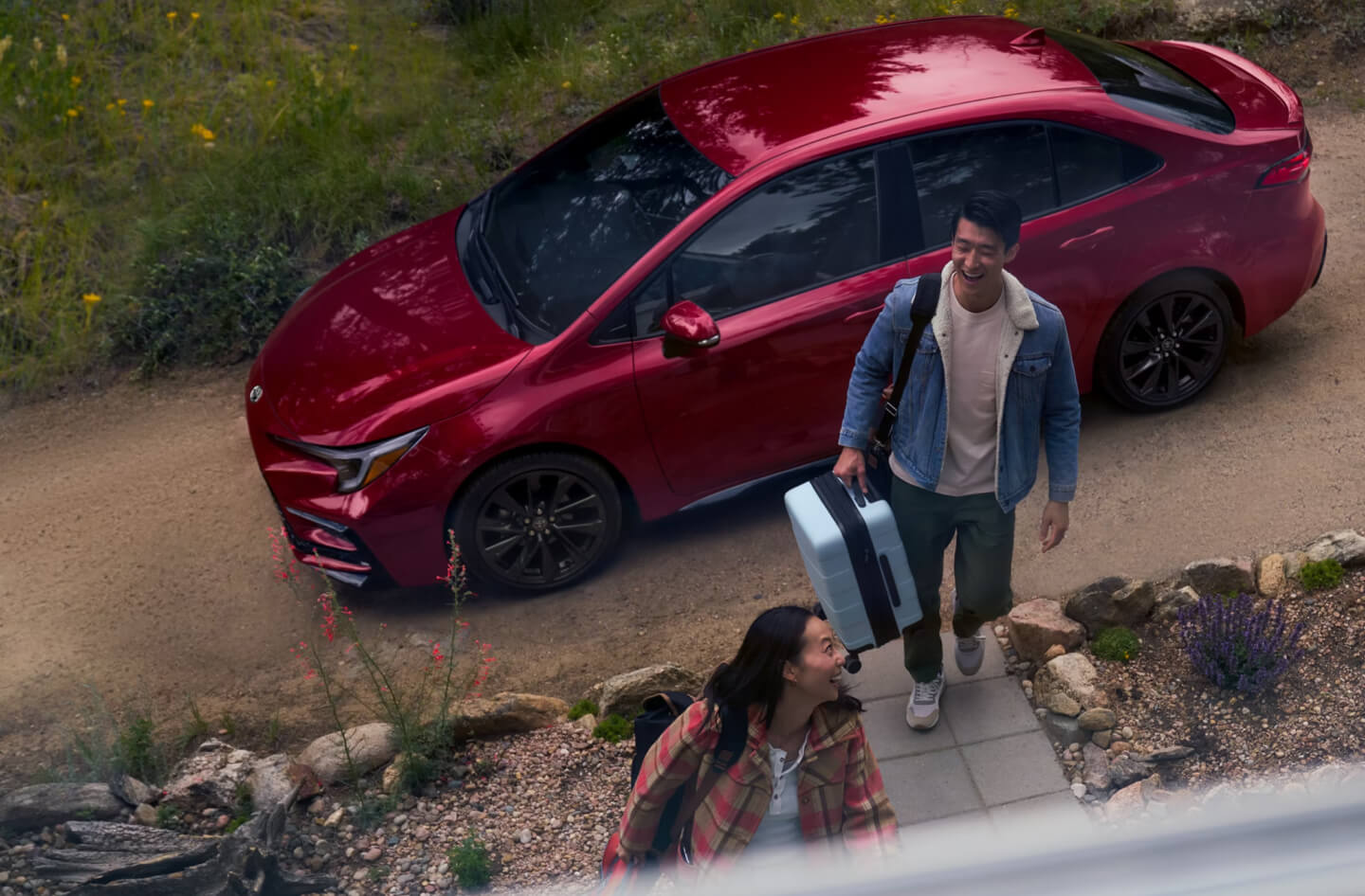 High-angle shot of a Toyota Corolla Hybrid in Red with a couple walking away on a stone path.